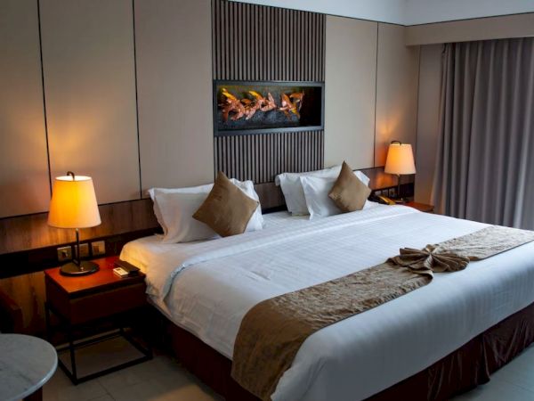 A well-appointed hotel room features a large bed with white linens, bedside tables with lamps, and a wall-mounted decorative element.