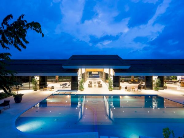 This image features a luxurious resort with a large, illuminated swimming pool, surrounded by modern architecture and outdoor seating areas.
