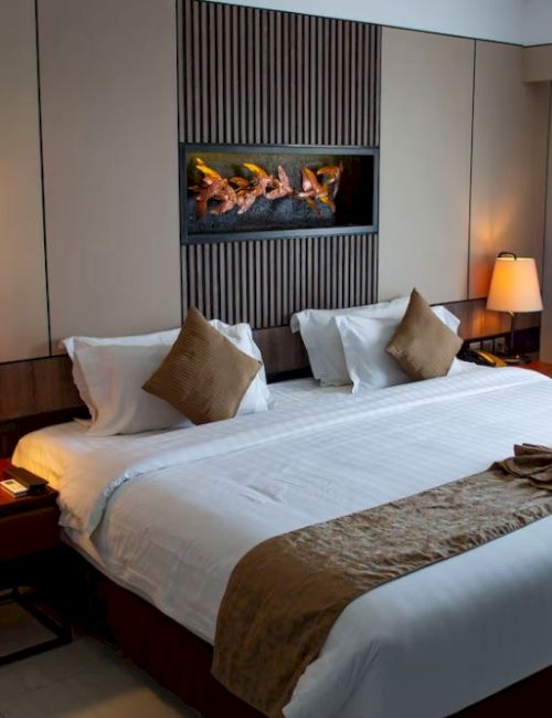 This image shows a well-lit hotel room with a large bed, bedside tables with lamps, and a modern decor. The bed features pillows and a folded towel.