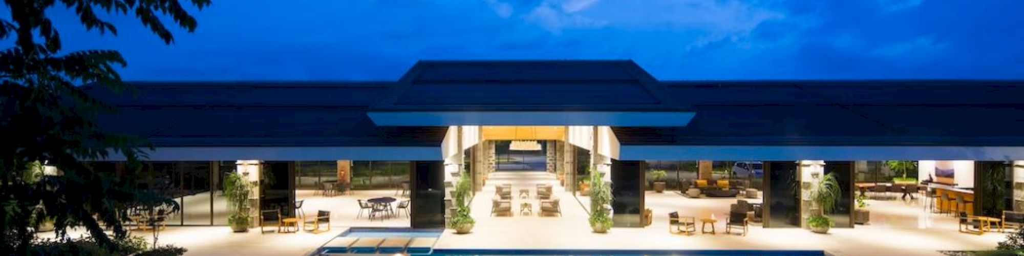 A luxurious resort at dusk features an inviting outdoor pool reflecting the elegant architecture and ambient lighting of the building.