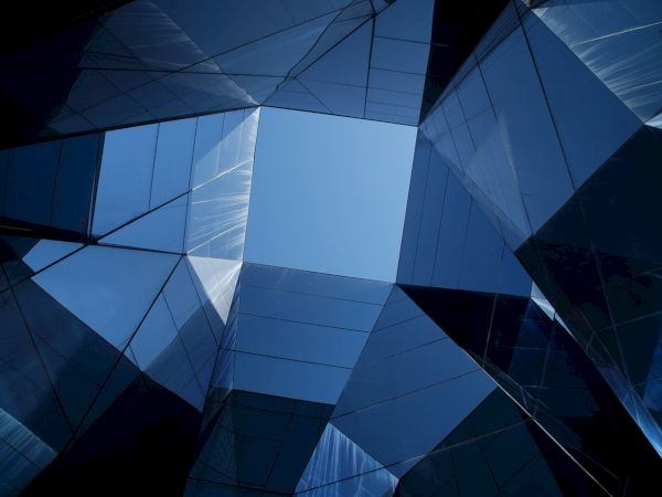 This image shows a series of intersecting glass surfaces forming a geometric pattern, with a clear blue sky visible through the opening at the center.