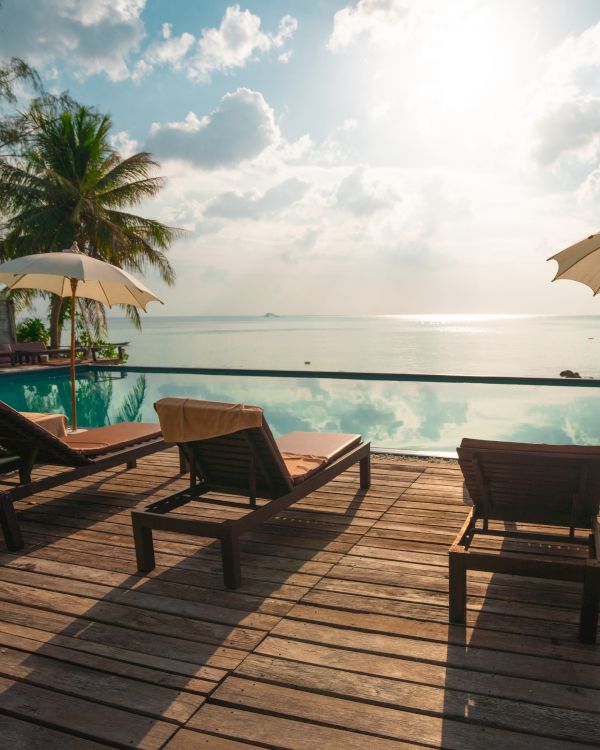 A serene beach scene featuring lounge chairs, umbrellas, and a pool by the water, with a stunning view of a tropical paradise under a bright sky.