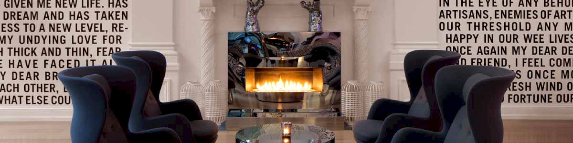 The image shows a modern living room with a fireplace, text-covered walls, dark blue chairs surrounding a glass table, and a chandelier above.