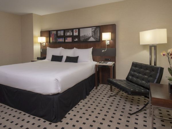 A modern hotel room features a large bed, a black chair, bedside tables with lamps, and a small table with a potted orchid.