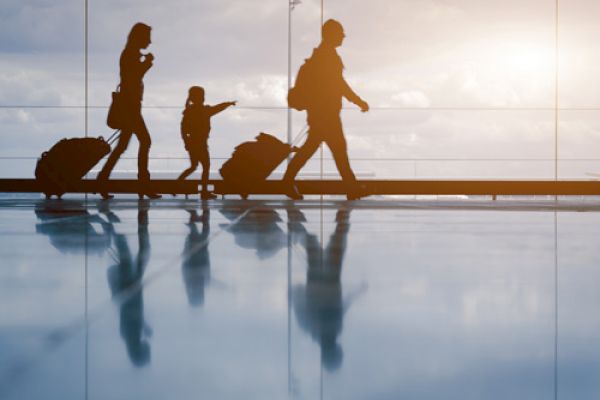 Silhouette of a family with luggage walking in an airport during sunset, reflecting on the shiny floor while a child points ahead.