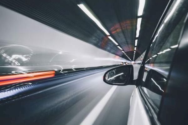 A car speeds through a tunnel, creating light trails and a sense of motion. The image is taken from the side window, showing the side mirror.