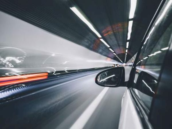 A car speeds through a tunnel, creating light trails and a sense of motion. The image is taken from the side window, showing the side mirror.