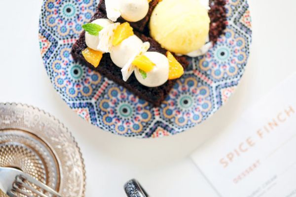 A dessert plate with cake topped with cream, fruit, and ice cream, next to cutlery and a glass plate. A 