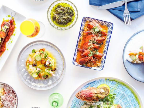 The image shows a variety of colorful dishes on a table, including seafood, salads, and sauces, with cutlery and a napkin to the side.