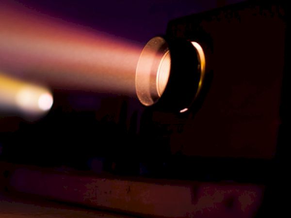 The image shows a projector emitting a beam of light, creating a colorful glow in a dark room.