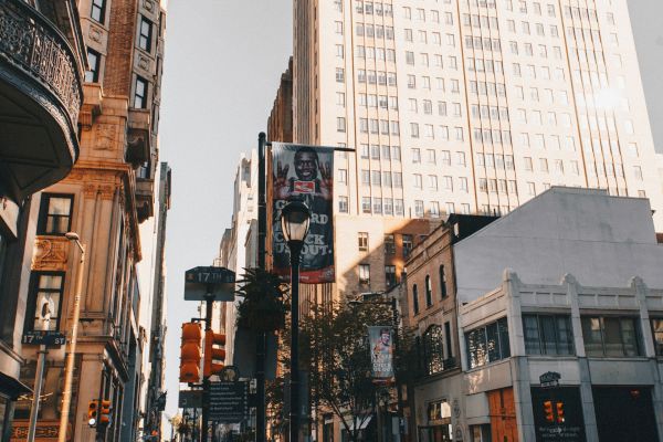 A busy city street with tall buildings, people walking, and a few stores; the sky is clear and the scene is vibrant and dynamic, capturing urban life.