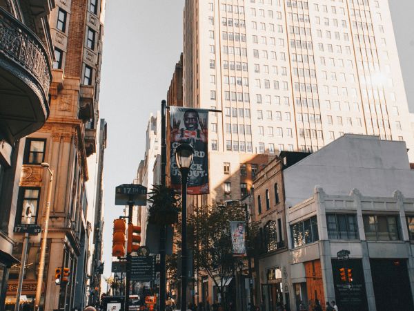 A busy city street with tall buildings, people walking, and a few stores; the sky is clear and the scene is vibrant and dynamic, capturing urban life.