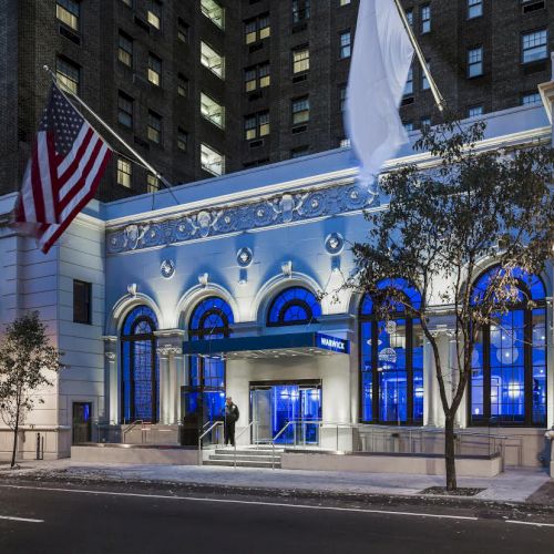 The image shows the illuminated entrance of a building with American and white flags, trees, and a lit streetlamp at night.