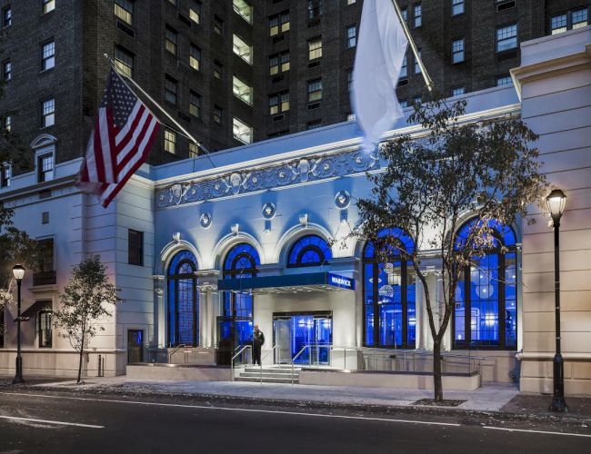 The image shows the illuminated entrance of a building with American and white flags, trees, and a lit streetlamp at night.