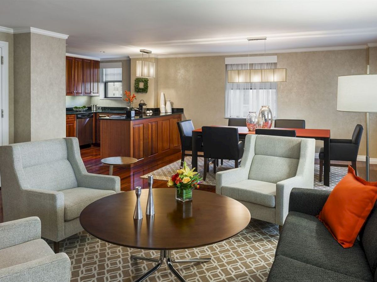 A modern living room with comfortable seating, a round coffee table, a dining area, and an open kitchen with wooden cabinets.