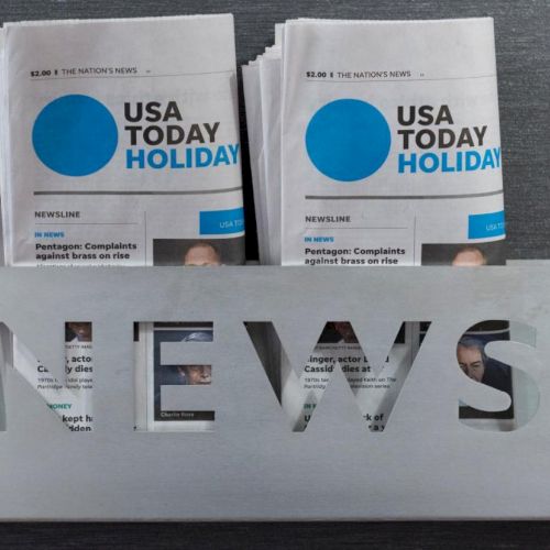 The image shows a metal newspaper holder with the word 