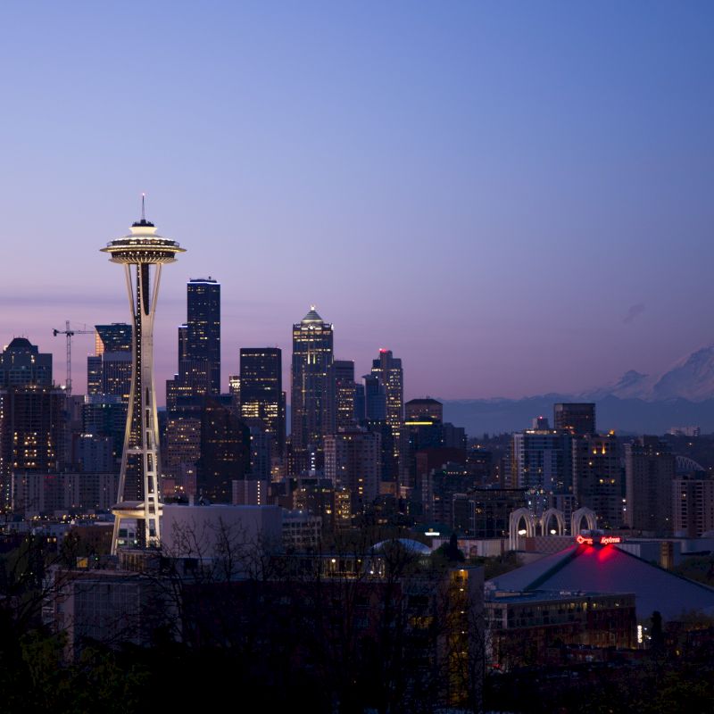 This image shows the Seattle skyline at twilight, featuring the iconic Space Needle and Mount Rainier in the background.