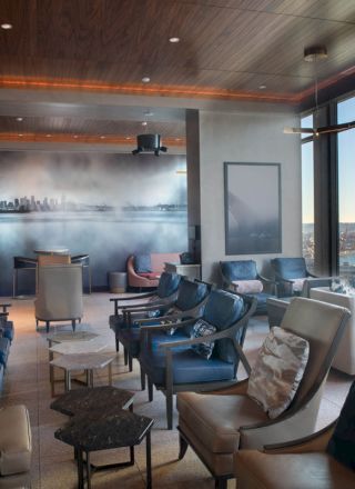A modern lounge area with comfortable seating, large windows offering a scenic view of the sea, and wall art of a skyline.
