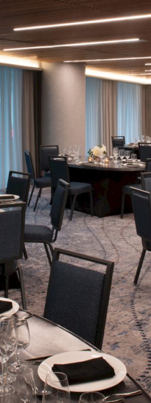 The image shows an elegant banquet hall set up for an event, with round tables covered in black linens, set with wine glasses, plates, and napkins.
